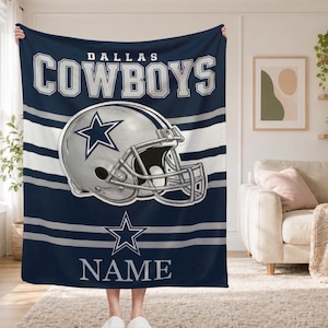 May include: A navy blue fleece blanket featuring the text DALLAS COWBOYS in white and silver, a central graphic of a silver football helmet with a blue star, and a large blue star above the word NAME printed in white at the bottom of the blanket.