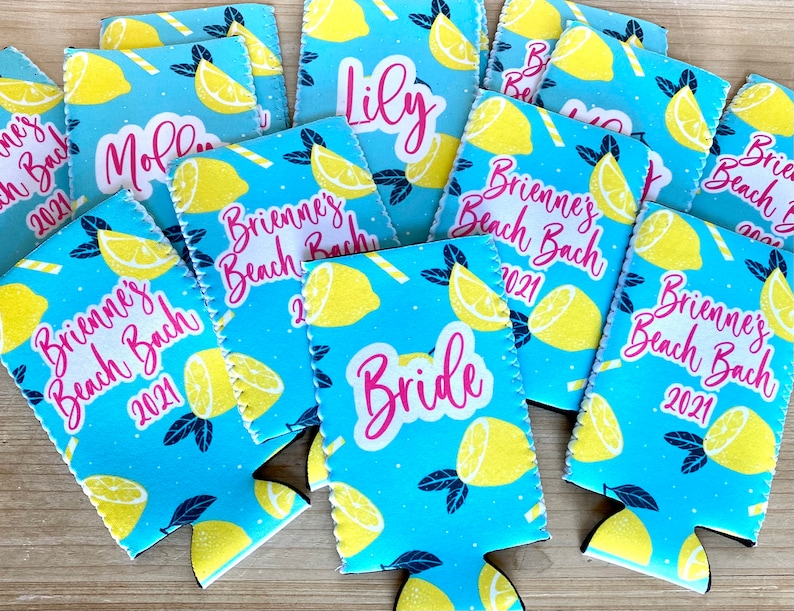May include: A collection of blue drink koozies with a lemon pattern. The koozies have text that reads "Brienne's Beach Bach 2021", "Bride", "Lily", and "Mollie". The koozies are made of a soft, insulating material.