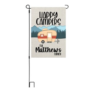 May include: A garden flag with a vintage camper illustration, mountains, and trees. The text reads "Happy Campers" and "The Matthews Family".