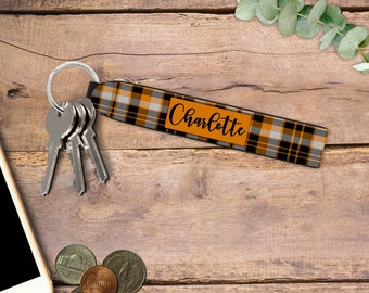 May include: A black and orange plaid keychain with a silver key ring and the name "Charlotte" printed on it.