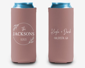 May include: Two pink can coolers with white text. The first cooler says "the JACKSONS 11.20.21" with a floral wreath around the text. The second cooler says "Kayla + Derek -VALDOSTA, GA- "