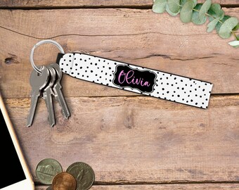 May include: A white and black polka dot key chain with a black frame and the name "Olivia" written in pink lettering.