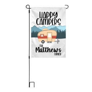 May include: A white garden flag with a cartoon illustration of a vintage camper, mountains, and trees. The text "Happy Campers" is at the top of the flag, and the text "The Matthews Family" is at the bottom.