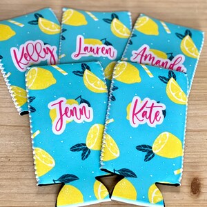 May include: Five personalized drink koozies with a light blue background and a pattern of yellow lemons and white and yellow straws. Each koozie has a different name in pink script: Kelly, Lauren, Amanda, Jenn, and Kate.