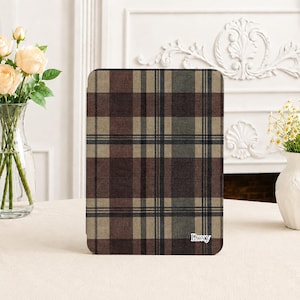 May include: A rectangular tablet case featuring a brown, tan, and dark green plaid pattern with a textured fabric-like appearance. The word Roxy is printed in white, sans-serif capital letters in the bottom right corner of the front cover.