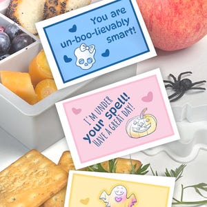 Puede incluir: Tres tarjetas rectangulares imprimibles con temas de Halloween. Una tarjeta azul dice You are un-boo-lievably smart! con una calavera. Una tarjeta rosa dice I'M UNDER your spell! HAVE A GREAT DAY! con una calabaza. Una tarjeta amarilla dice YOU ARE FA-BOO-LOUS! con un fantasma.