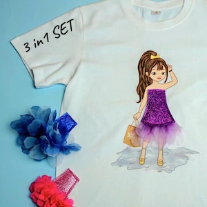 Pode incluir: Uma t-shirt branca de manga curta com o texto 3 in 1 SET e um gráfico de uma personagem de cabelo castanho com um vestido roxo brilhante e um saco de compras, acompanhada por um gancho de cabelo azul e um rosa em forma de flor.