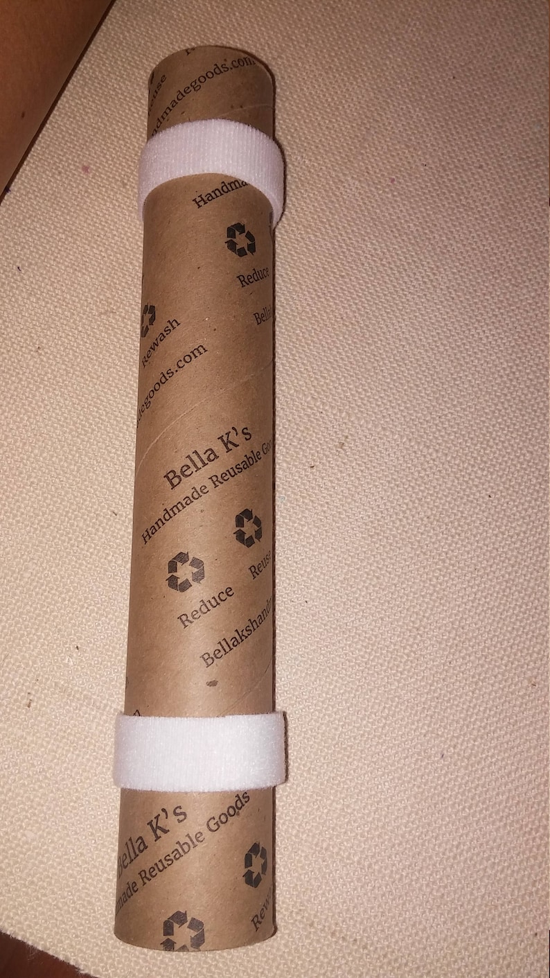May include: A brown cardboard tube with white tape wrapped around it. The tube has the text "Bella K's Handmade Reusable Goods" printed on it, along with a recycling symbol and the words "Reduce, Reuse, Bellakshandmadegoods.com".