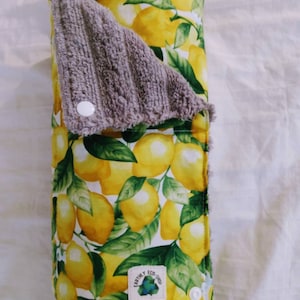 May include: A reusable paper towel made of fabric with a lemon print. The towel is rolled up and has a gray terry cloth side. The towel has a white label with the text "Earthly Eco Shop".