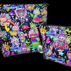 May include: Two black zippered pouches with a colorful cartoon design. The design features whimsical characters, including bunnies, in a vibrant array of colors. The pouches are ideal for storing cosmetics or other small items.