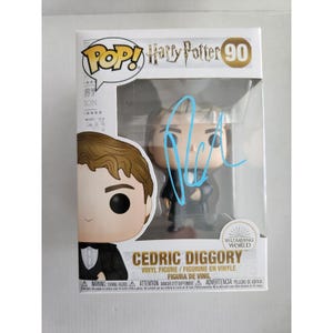 Könnte beinhalten: Eine Funko Pop Harry Potter Cedric Diggory Vinylfigur, Nummer 90, in ihrer Originalverpackung. Die Schachtel zeigt den Charakternamen, das Wizarding World Logo und ein hellblaues Autogramm auf dem durchsichtigen Kunststofffenster.