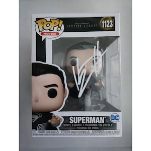 May include: A Funko Pop Movies vinyl figure of Superman from Zack Snyder's Justice League, numbered 1123. The box features a black and white suit character design, a clear display window, and a white autograph written across the plastic front.