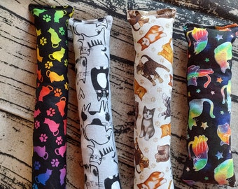 May include: Four cat-themed catnip toys. The toys are long and narrow, with different patterns. One toy has a rainbow pattern, one has a black and white cat pattern, one has a brown and white cat pattern, and one has a colorful cat pattern.