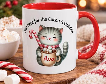 Peut inclure: Un mug en céramique blanc avec un intérieur et une anse rouges, illustré d'un chat tigré gris tenant une canne en sucre et une tasse marquée Ava, avec le texte Just Here for the Cocoa & Cuddles imprimé en noir au-dessus du chat.
