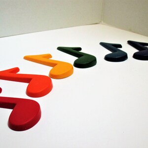 May include: A set of seven musical note shaped crayons in a rainbow of colours, including red, orange, yellow, green, blue, indigo, and violet.