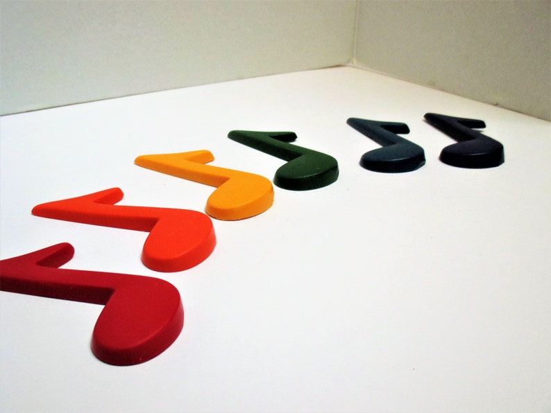 May include: A set of seven musical note shaped crayons in a rainbow of colours, including red, orange, yellow, green, blue, indigo, and violet.