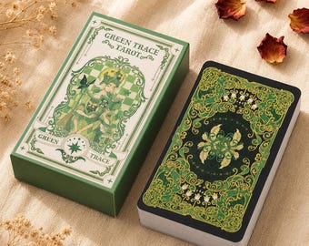Può includere: Un mazzo di tarocchi Green Trace composto da una scatola rettangolare con un'illustrazione verde e bianca di una figura che legge, e un mazzo di carte con un motivo floreale ornamentale verde scuro e oro sul retro, su tessuto.