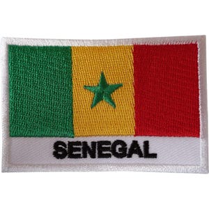 May include: A rectangular embroidered patch featuring the flag of Senegal with vertical green, yellow, and red stripes and a central green star. The word SENEGAL is embroidered in black capital letters on a white horizontal band at the bottom.