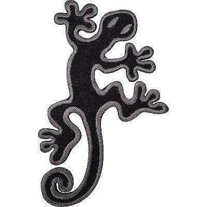 Könnte beinhalten: Ein gestickter Aufnäher in Form einer Eidechse mit einem einfarbig schwarzen Körper und einem markanten grauen Stickrand, der die gesamte Form nachzeichnet, einschließlich des geringelten Schwanzes und der gespreizten Zehen an allen vier Gliedmaßen.