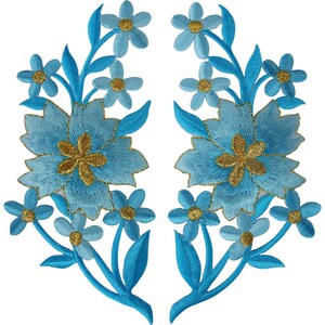 Könnte beinhalten: Zwei symmetrische Stickaufnäher mit hellblauen Blüten, goldenen Mitten und dunkelblauen Blättern. Jeder Aufnäher zeigt eine große zentrale Blüte, die von kleineren Blüten und Blattwerk umgeben ist, gefertigt mit detaillierter Stickerei.