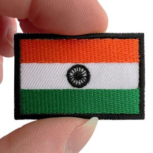 May include: A rectangular embroidered patch featuring the flag of India. The design consists of three horizontal bands in saffron, white, and green, with a black Ashoka Chakra wheel centered in the white band, all bordered by a thick black edge.