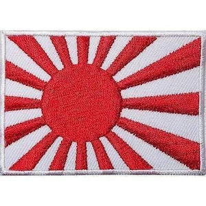 May include: A rectangular embroidered patch featuring the Japanese Rising Sun flag design. The patch displays a solid red circular centre with sixteen red rays extending outward against a white background, finished with a white stitched border.