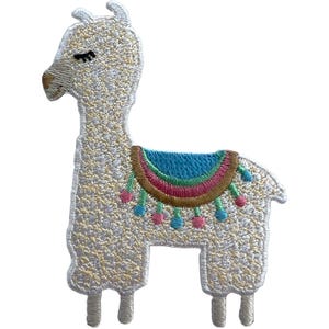 Puede incluir: Un parche bordado con forma de llama de pie con pelaje color crema, ojos cerrados y nariz marrón. La llama lleva una manta de silla de montar colorida con rayas horizontales en azul, rosa y marrón, decorada con pequeños pompones colgantes.