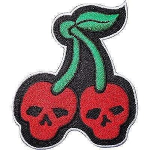 May include: An embroidered patch featuring two red cherry-shaped skulls with black eye sockets and nose cavities. The cherries are connected by green stems and a single green leaf, all outlined in black thread against a white border background.