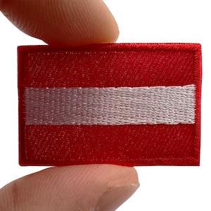 May include: A rectangular embroidered patch featuring the flag of Latvia, characterized by a horizontal white stripe centered between two wider horizontal red stripes, with a stitched border surrounding the entire rectangular design.