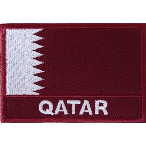 Puede incluir: Un parche rectangular bordado que muestra la bandera de Qatar con un fondo granate y una franja vertical blanca dentada en el lado izquierdo. La palabra QATAR está bordada en letras mayúsculas blancas sobre una barra granate en la parte inferior.