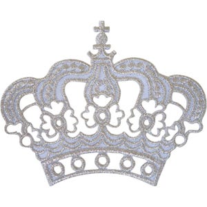 May include: A crown-shaped embroidered patch featuring a metallic silver thread design on a white fabric base. The intricate pattern includes floral-like cutouts, a scalloped lower edge with circular details, and a central cross-topped finial.