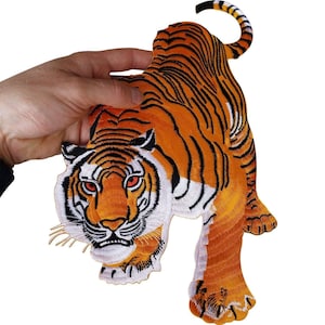 Op de afbeelding: Een geborduurde tijgerpatch met een feloranje lichaam met zwarte strepen, witte accenten op het gezicht en de buik, en doordringende rode ogen. De tijger is afgebeeld in een lopende houding met de staart omhoog gekruld en zichtbare klauwen.