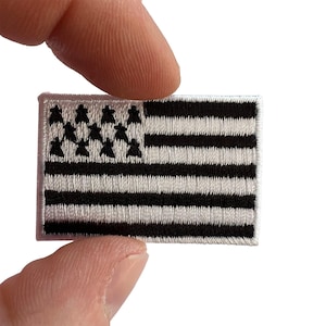 May include: A rectangular embroidered patch featuring the flag of Brittany, known as the Gwenn-ha-du. The design consists of nine alternating black and white horizontal stripes with a white canton in the upper left corner containing eleven black ermine spots.