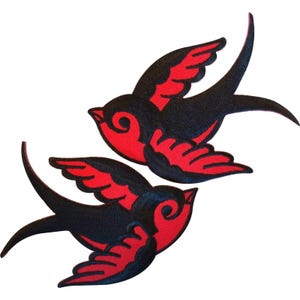 Puede incluir: Dos parches bordados de golondrinas con un diseño llamativo en hilo negro y rojo. Cada ave se muestra en pleno vuelo con las alas extendidas, exhibiendo costuras detalladas que definen las plumas y la forma del cuerpo con gran contraste.