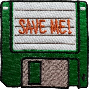 Puede incluir: Un parche bordado con forma de disquete cuadrado. El disquete es verde con una etiqueta blanca que presenta el texto naranja SAVE ME! en estilo manuscrito. Un obturador deslizante de metal gris es visible en la parte inferior del marco verde.