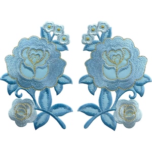Könnte beinhalten: Zwei identische gestickte Aufnäher mit einer großen, hellblauen Rose in der Mitte, die mit goldenen Fäden verziert ist und von kleineren hellblauen Blüten und Blättern umgeben wird. Die Stickerei ist dicht mit einem Satinstich-Finish und zeigt komplexe florale Muster in Blau- und Goldtönen auf weißem Hintergrund.