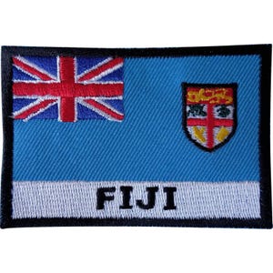 May include: A rectangular embroidered patch featuring the flag of Fiji with a light blue field, a Union Jack in the upper left corner, and the Fiji shield on the right. The word FIJI is embroidered in bold black capital letters on a white band.