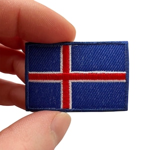 Puede incluir: Un parche rectangular bordado que muestra la bandera de Islandia. El diseño consiste en un fondo azul oscuro con una cruz roja delineada en blanco, con un borde cosido que enmarca toda la forma rectangular del parche.