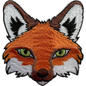 Pode incluir: Um emblema bordado apresentando a cabeça de uma raposa com olhos verde-brilhantes. A raposa tem pelo laranja na testa e nas bochechas, pelo branco ao redor do focinho e nas orelhas, e detalhes em marrom escuro e preto nas orelhas e nariz.