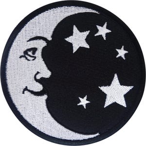 Peut inclure: Un écusson brodé circulaire présentant un croissant de lune blanc avec un profil de visage humain sur le côté gauche, sur un fond noir. Le motif comprend quatre étoiles blanches à cinq branches de tailles variées dispersées à droite.