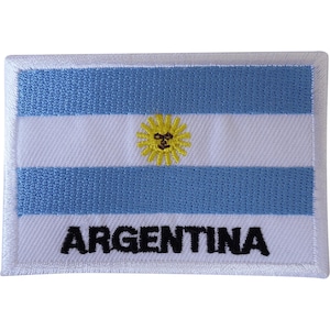 May include: A rectangular embroidered patch featuring the flag of Argentina with two light blue horizontal stripes and a central white stripe. A yellow sun with a face is centred in the white stripe. The word ARGENTINA is stitched in black.