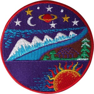 Pode incluir: Um emblema bordado circular apresentando um céu noturno roxo com uma lua crescente, estrelas e um planeta com anéis sobre uma paisagem de montanhas nevadas, um rio azul, árvores verdes e um sol laranja brilhante sobre a água.