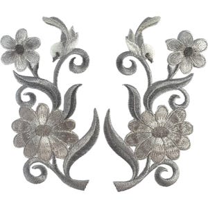 Puede incluir: Un par de parches bordados con motivos florales en tono plateado, que presentan dos cabezas de flores distintas, tallos curvos y patrones de hojas en espiral. El intrincado trabajo de hilo crea una apariencia metálica texturizada.