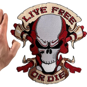 May include: A large embroidered patch featuring a central skull design in shades of grey and red, flanked by crossed bones. A beige banner arches over the top and bottom with the red embroidered text "LIVE FREE" and "OR DIE" respectively.