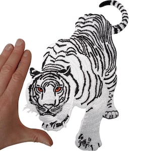 Può includere: Una toppa ricamata raffigurante una tigre bianca con strisce nere e occhi rossi penetranti. La tigre è raffigurata in una posa in agguato con la coda curva verso l'alto. Il design è realizzato con un dettagliato lavoro di ricamo.