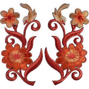 Op de afbeelding: Twee symmetrische geborduurde patches met oranje en rode bloemmotieven. Elke patch toont een grote onderste bloem, een kleinere bovenste bloem en krullende, rankachtige stengels met puntige bladeren in tinten donkerrood en feloranje.