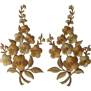 May include: A pair of symmetrical gold-colored embroidered floral appliques. Each piece features a central stem with multiple five-petaled blossoms and pointed leaves, rendered in a metallic thread with a dense, textured stitch pattern.