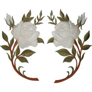 Puede incluir: Un par de parches bordados simétricos que presentan rosas blancas con capullos cerrados, hojas verdes y tallos marrones. El diseño floral está detallado con costuras intrincadas, mostrando una disposición curva de pétalos y follaje.