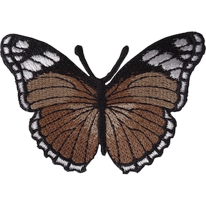 Peut inclure: Un écusson brodé en forme de papillon avec un centre marron, des bordures d'ailes noires et des accents blancs sur les bords. Le motif comprend deux antennes noires et des coutures détaillées sur toutes les ailes, créant un aspect texturé.
