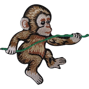 Puede incluir: Un parche bordado que muestra un mono de color marrón y bronceado con la cara y las orejas claras. El mono aparece en una pose dinámica, sosteniendo con ambas manos una fina enredadera verde horizontal que cruza su cuerpo.